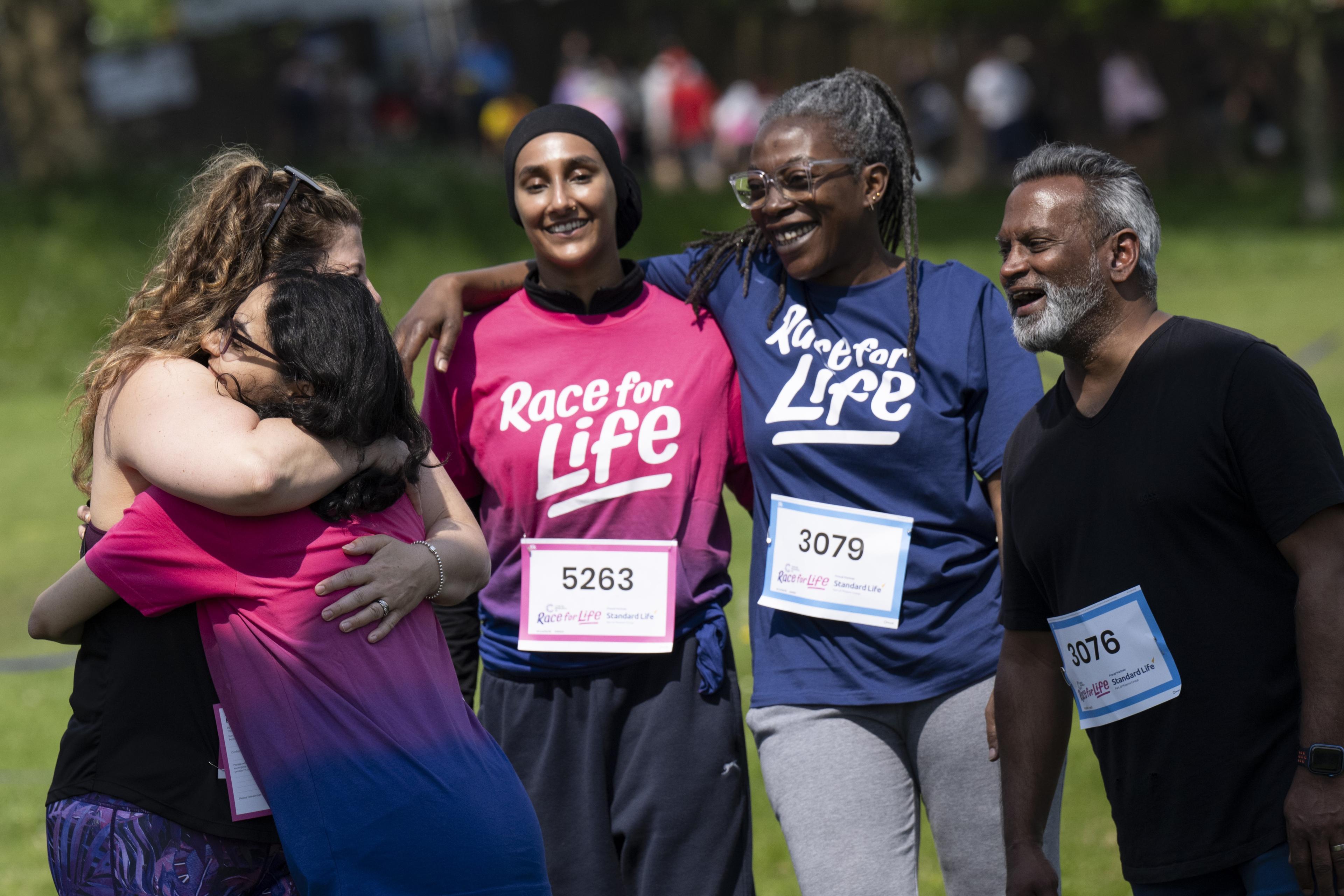 A photo of a group of five runners wearing Race for Life T-shirts, smiling together. Two of the runners are hugging.