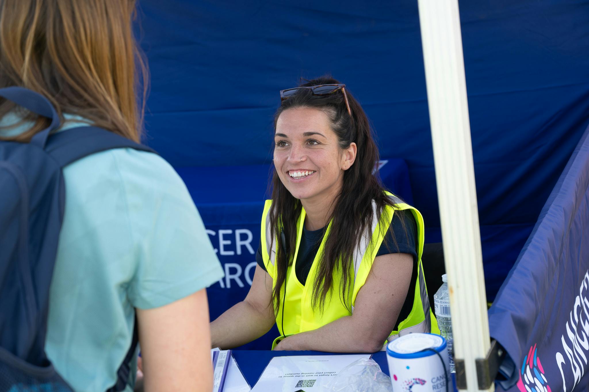 A Race For Life volunteer wearing a hi vis jacket and helping someone at the event check-in tent.