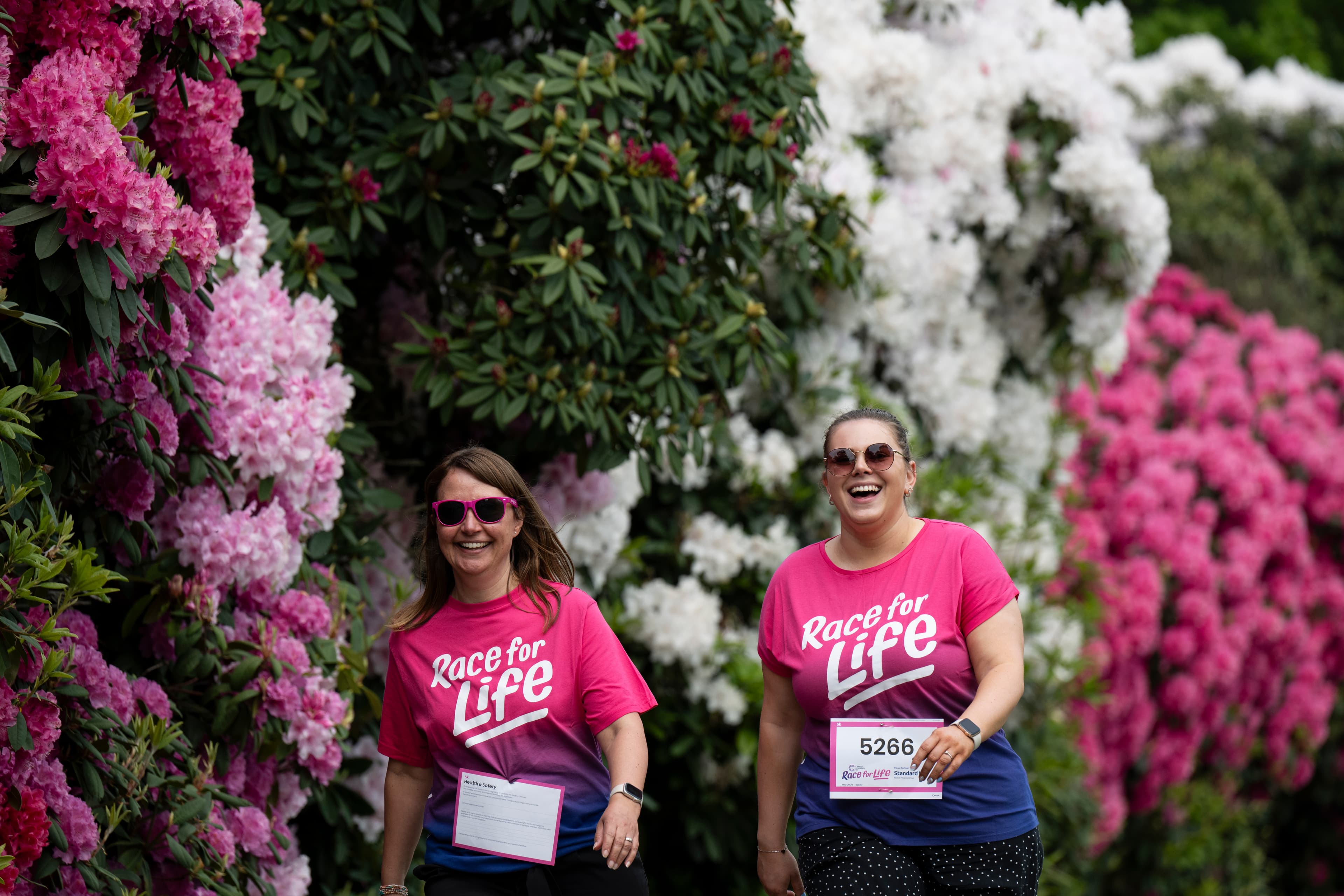 Race for Life participants walking and smiling in a park. Both wearing Race for Life t-shirts.