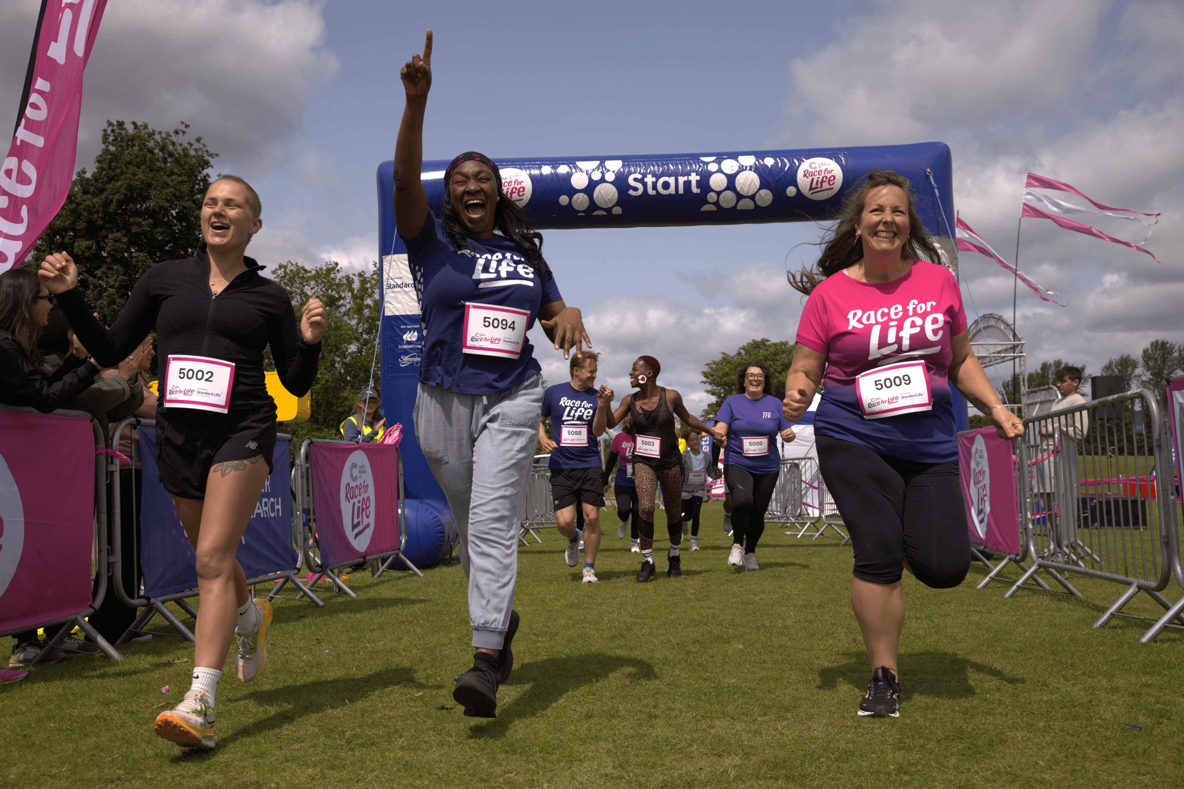 a group wearing Race for Life T-shirts beginning their race at the start line with smiles on their faces.