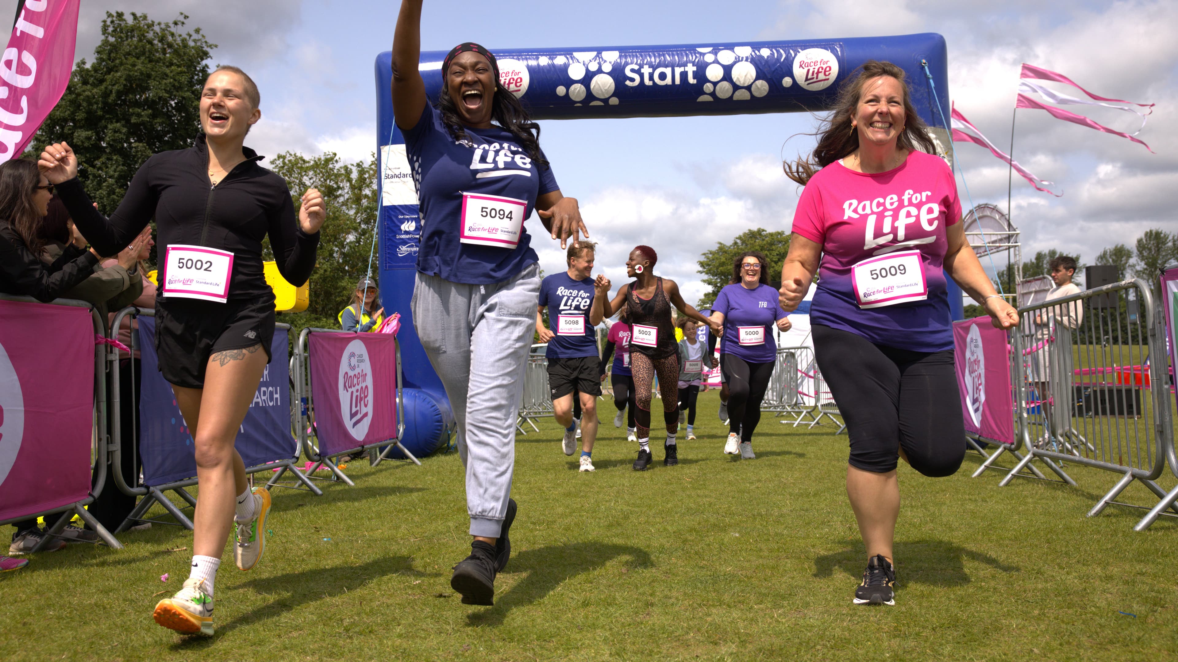 a group wearing Race for Life T-shirts beginning their race at the start line with smiles on their faces.