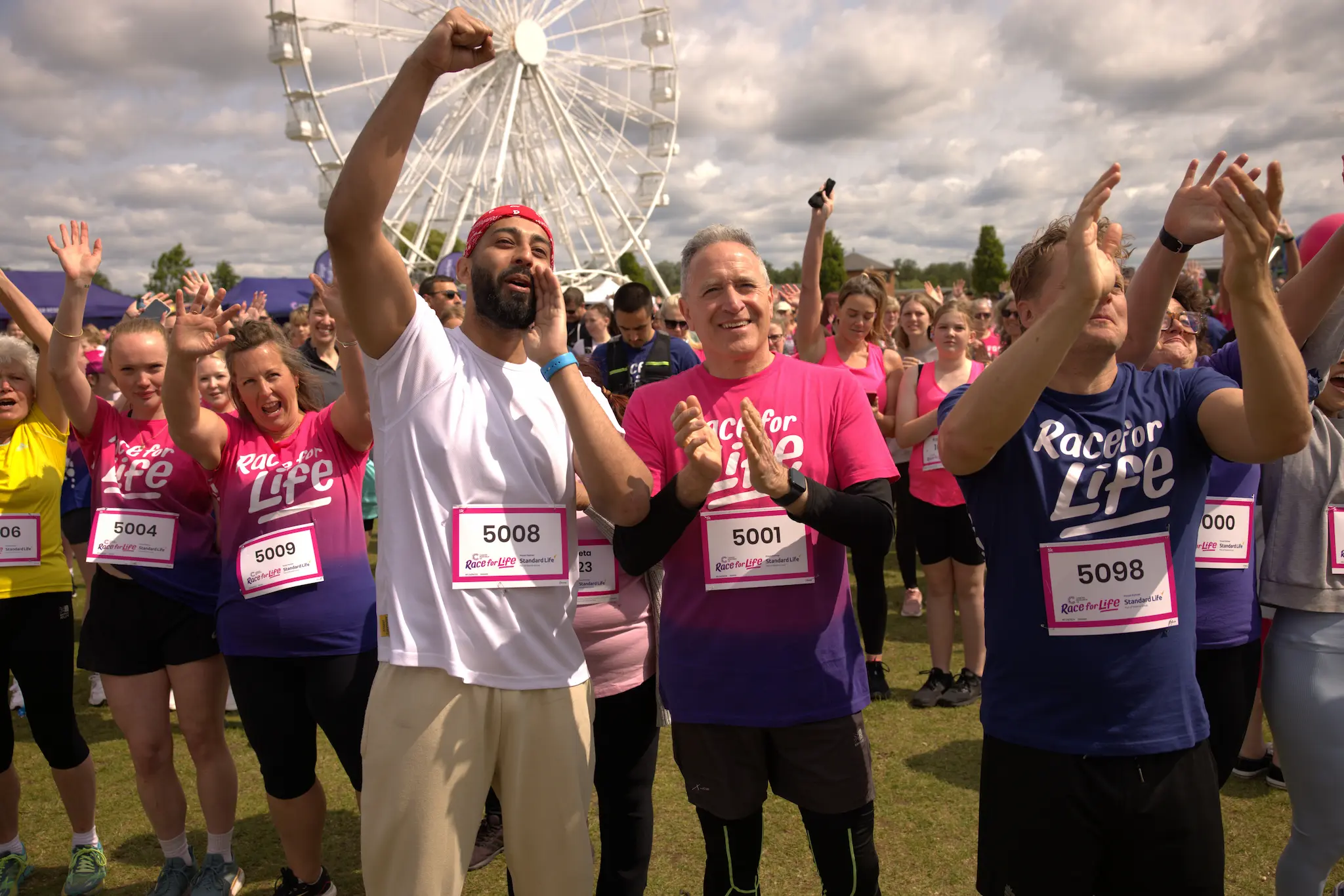 A crowd of people taking part in race for life cheering and clapping.