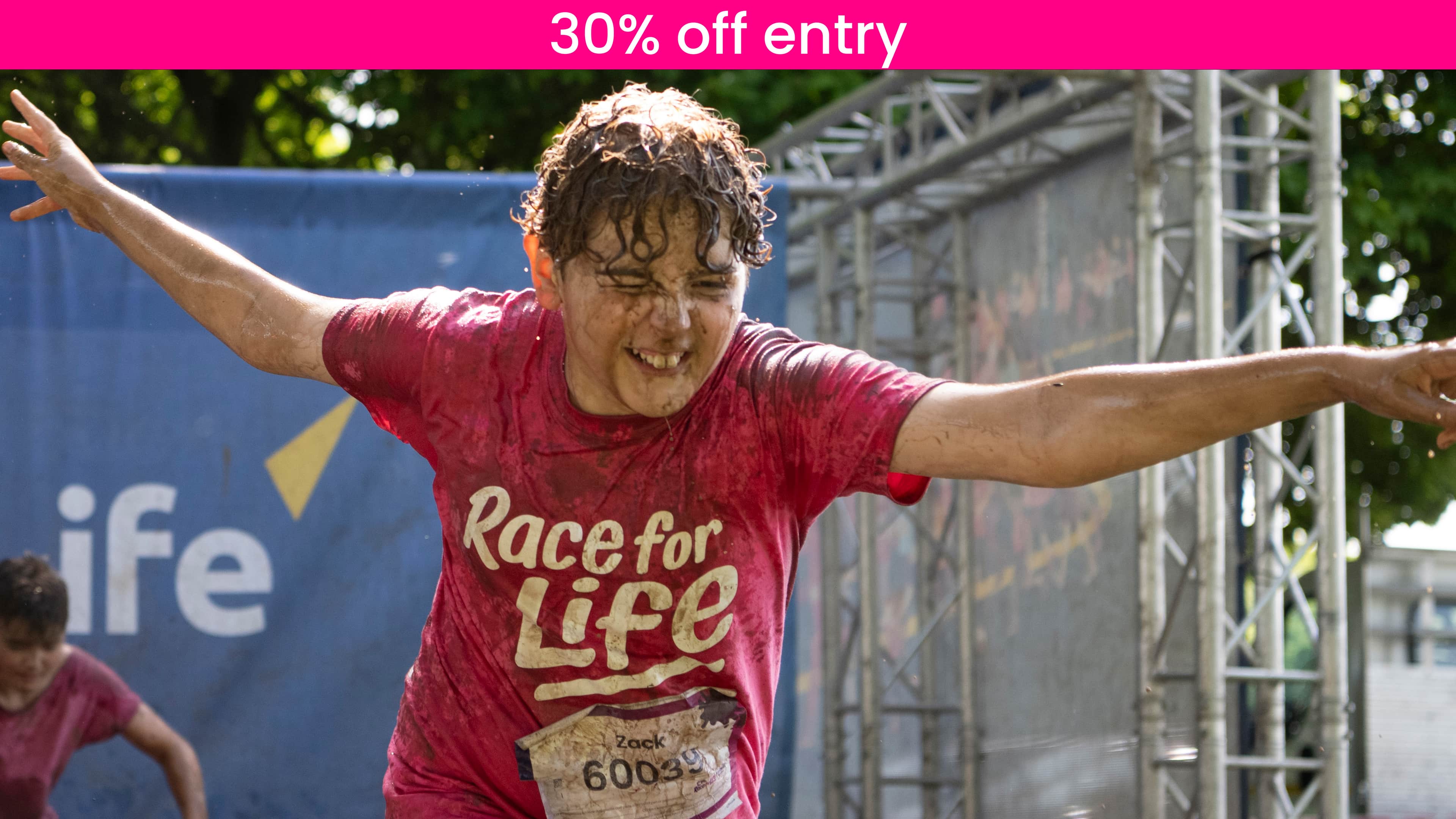 A young boy is having fun taking part in a Pretty Muddy Kids race. He is wearing a pink T-shirt and covered in muddy water.