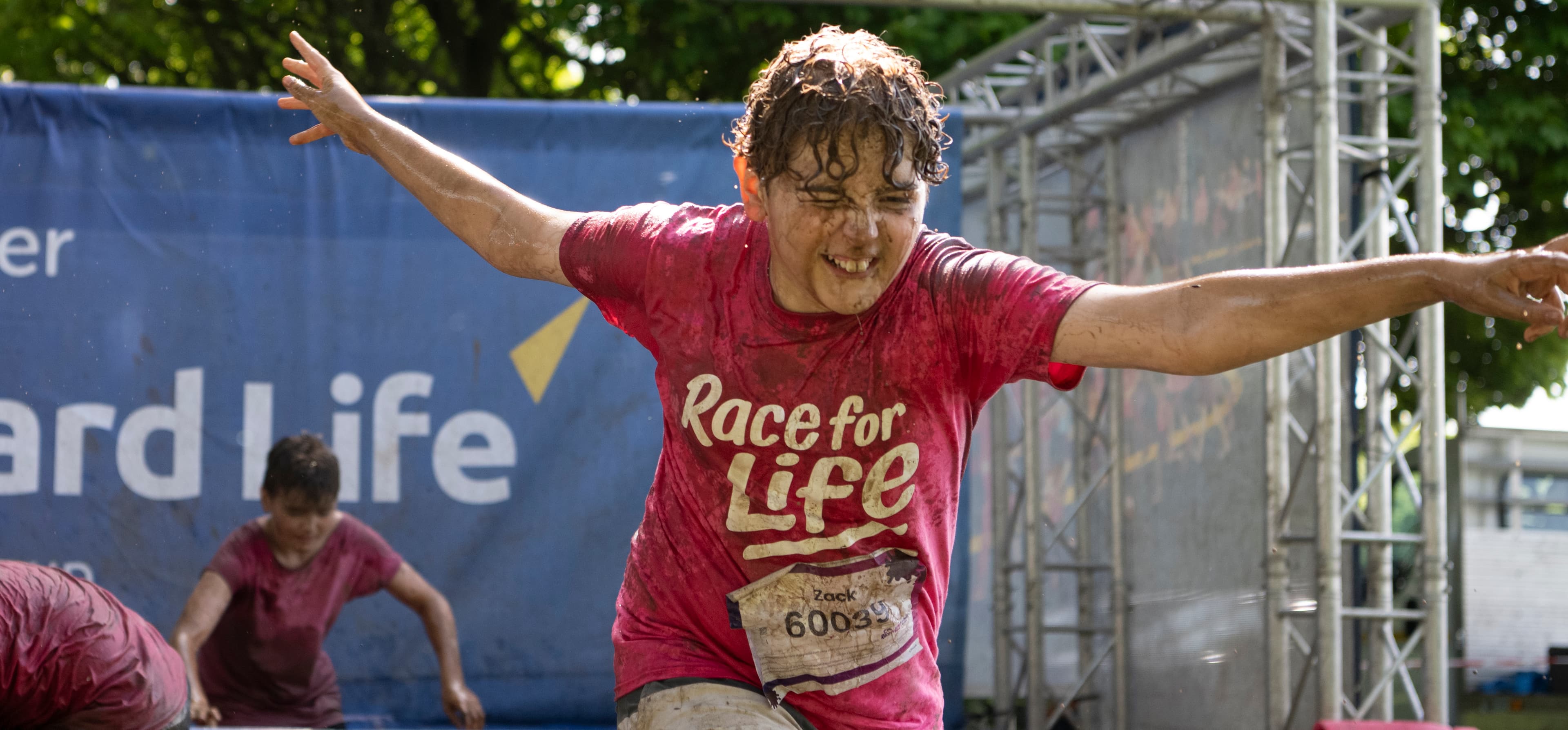A young boy is having fun taking part in a Pretty Muddy Kids race. He is wearing a pink T-shirt and covered in muddy water.