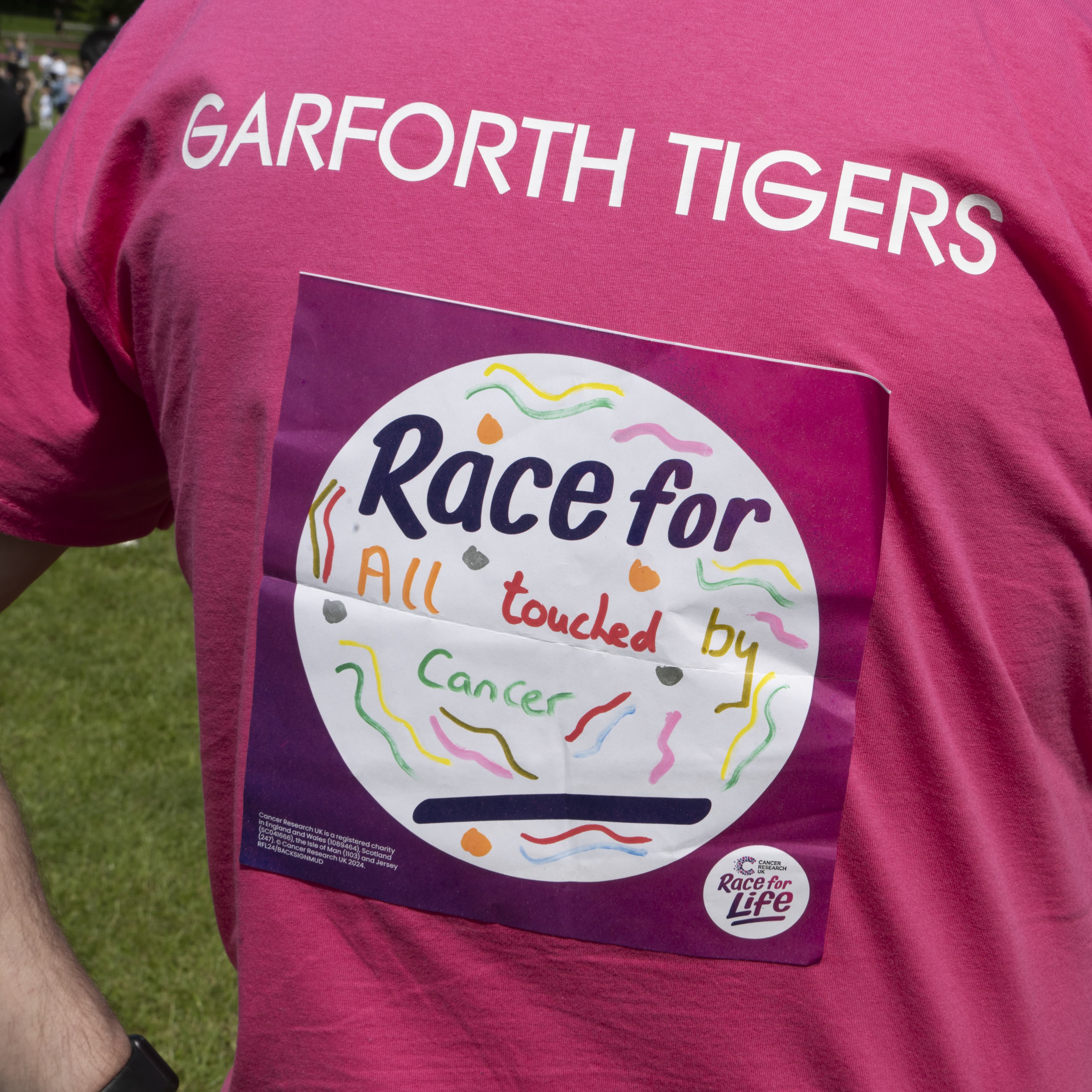A Race for Life runner's back sign which says 'Race for all toughed by cancer'.