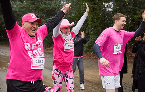 Three Race for Life participants. As they run they're smiling and have their arms in the air.