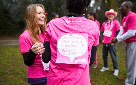 Race for Life runners wearing pink. One has a back sign which says I am running for Steve who is beating prostate cancer.