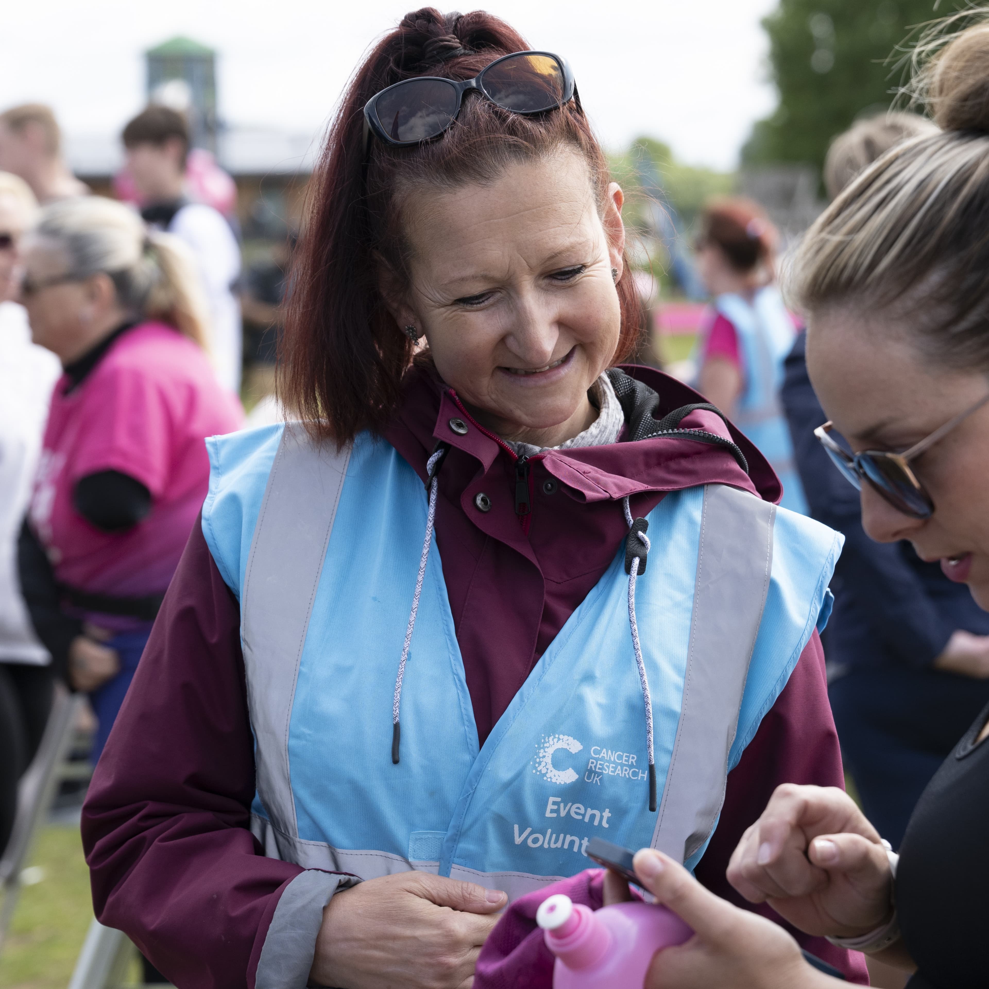 A Race For Life volunteer wearing a hi vis jacket and helping someone at the event.