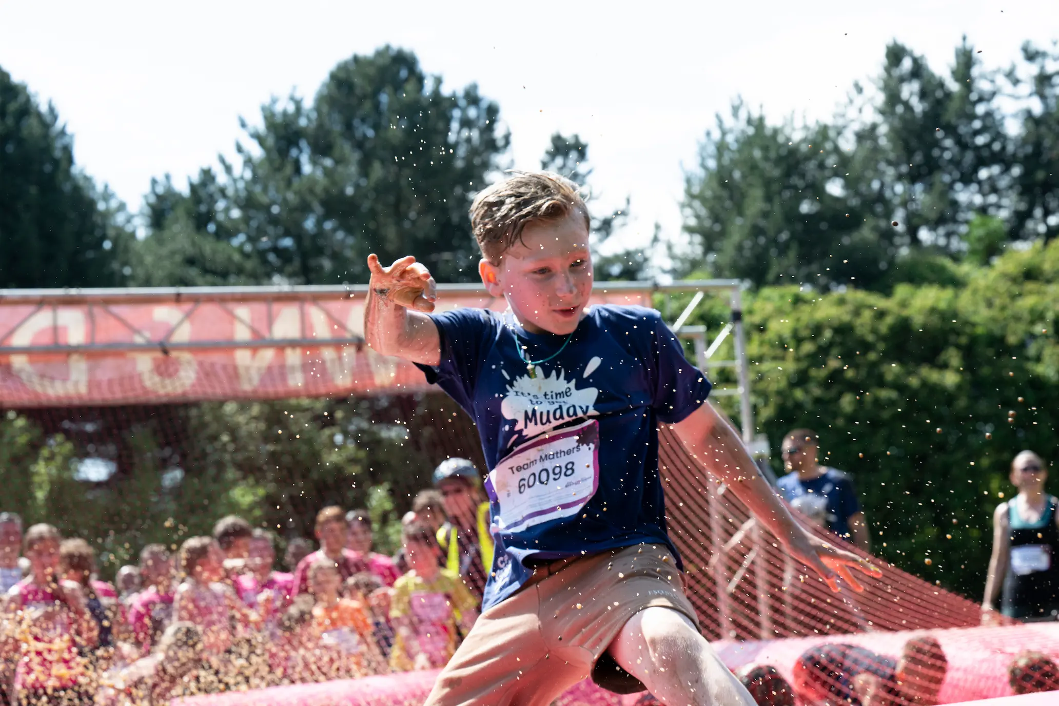A boy wearing a Pretty Muddy t-shirt jumping over a muddy obstacle.