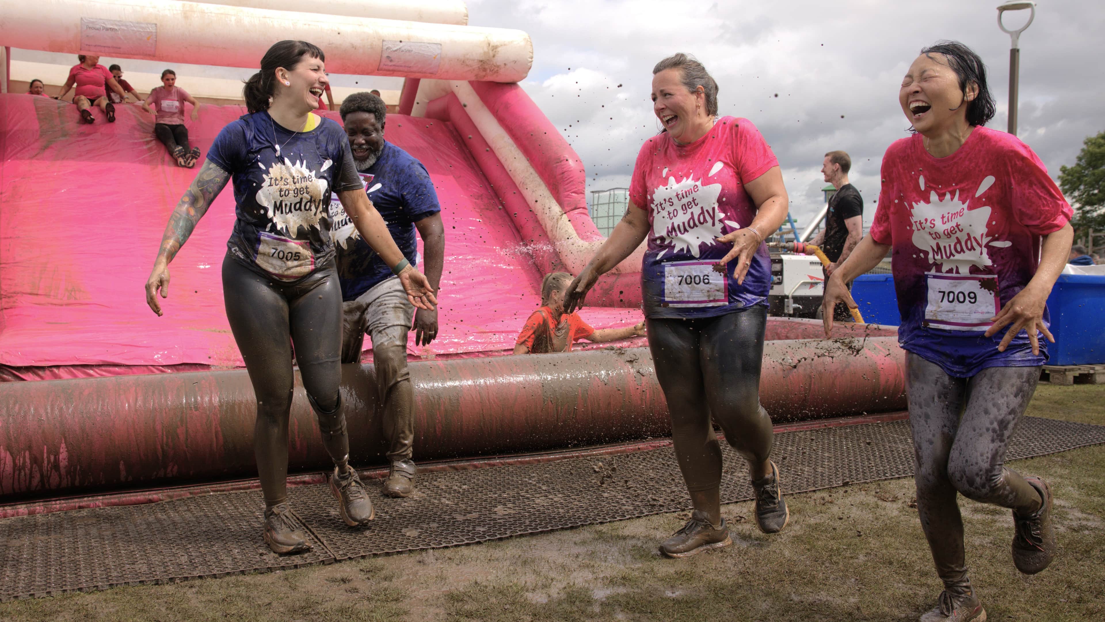 Group of women covered in mud at the bottom of the final muddy obstacle all laughing.