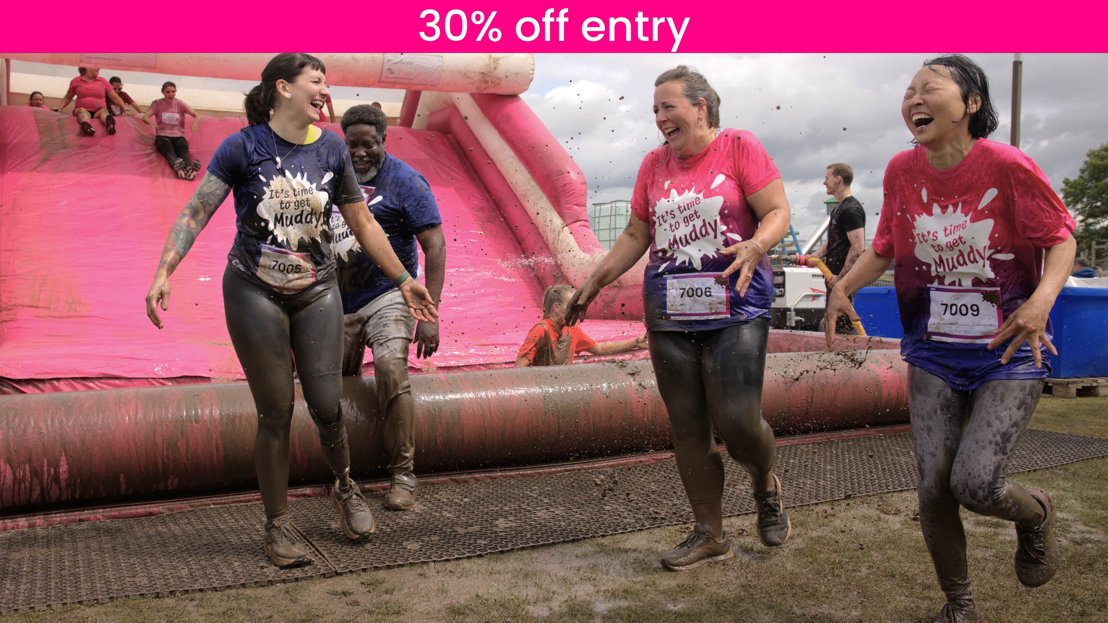 Group of women covered in mud at the bottom of the final muddy obstacle all laughing.