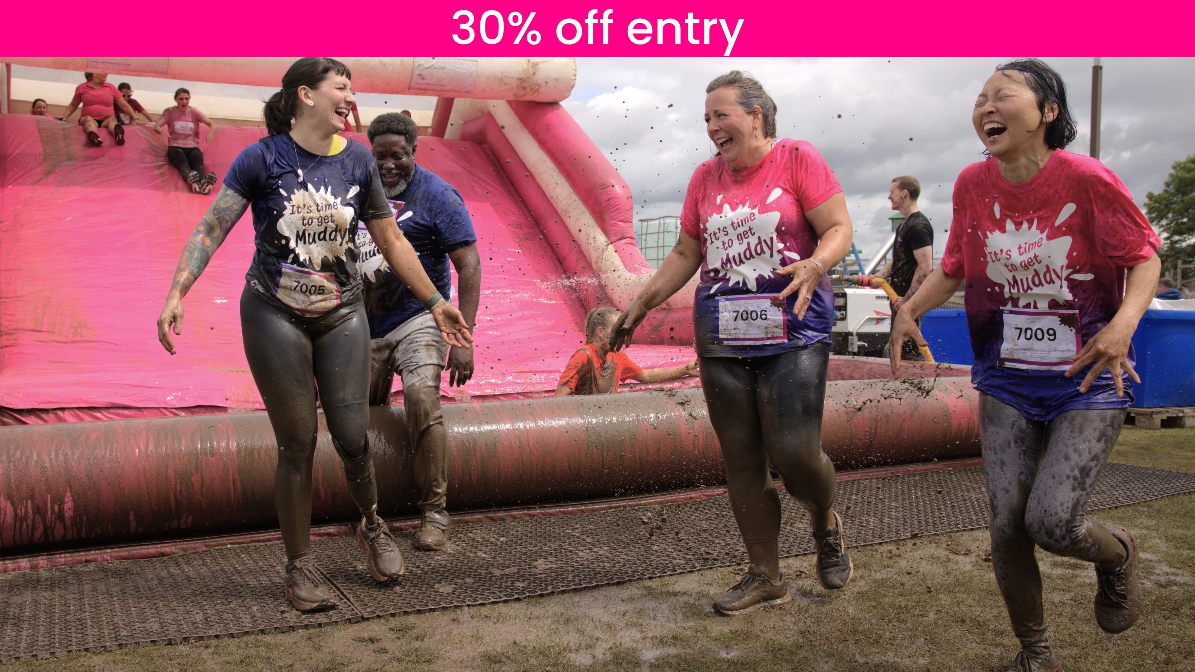 Group of women covered in mud at the bottom of the final muddy obstacle all laughing.