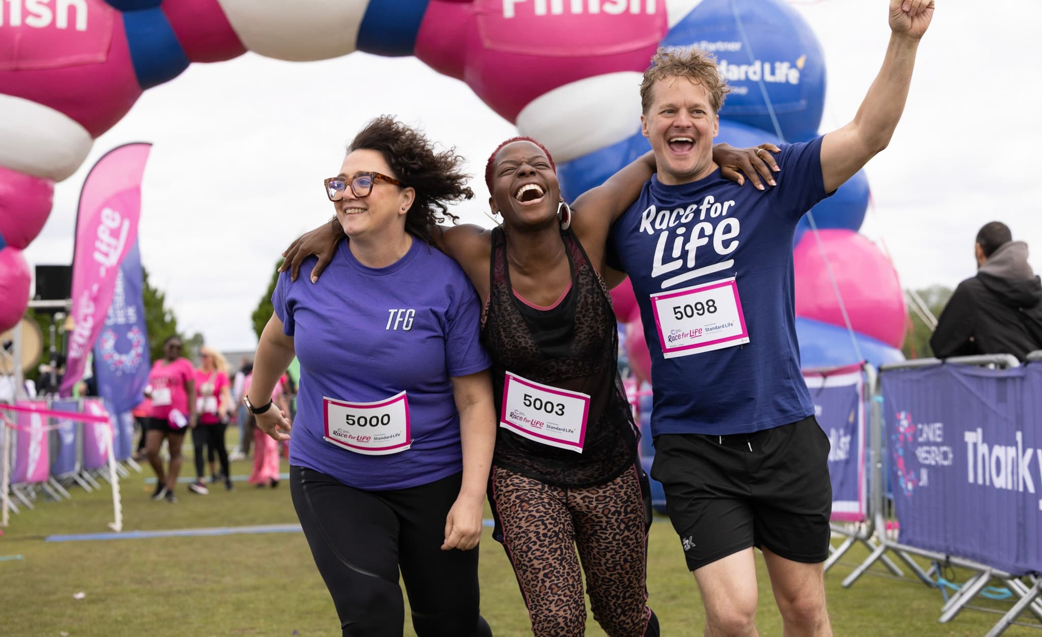 Three Race for Life participants running through the finish line together and laughing.