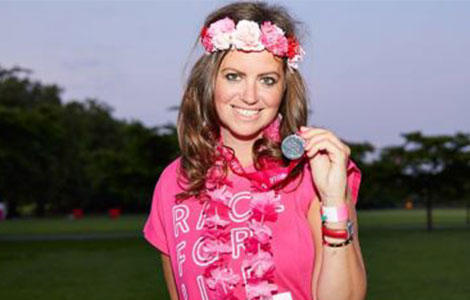 Dame Deborah James smiling wearing a flower crown and holding up a race for life medal