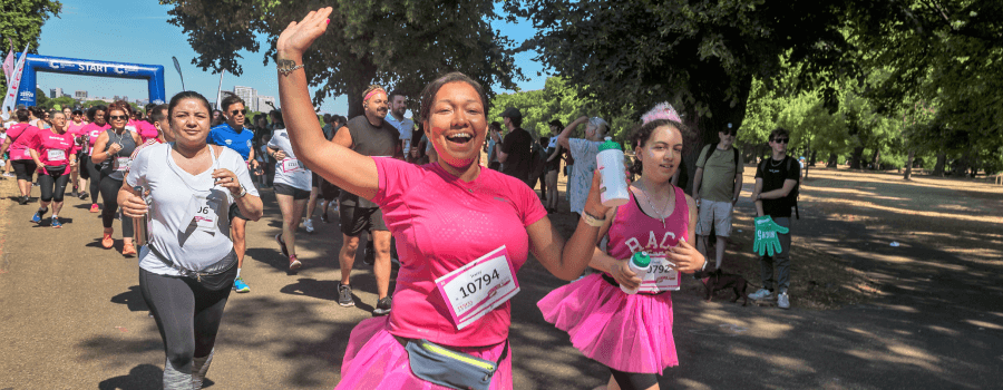 A woman wearing a pink t-shirt smiling and waving while running