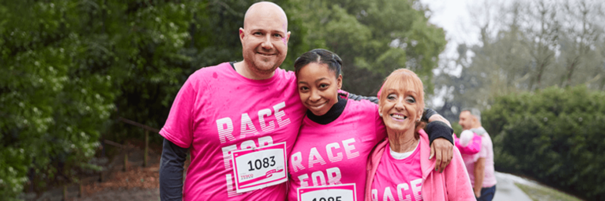 Three race for life participants smiling wearing pink t-shirts