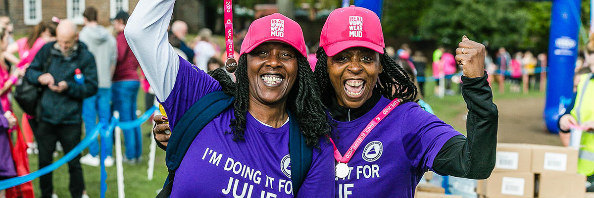 Two women smiling holding up their medals after completing a race for life event