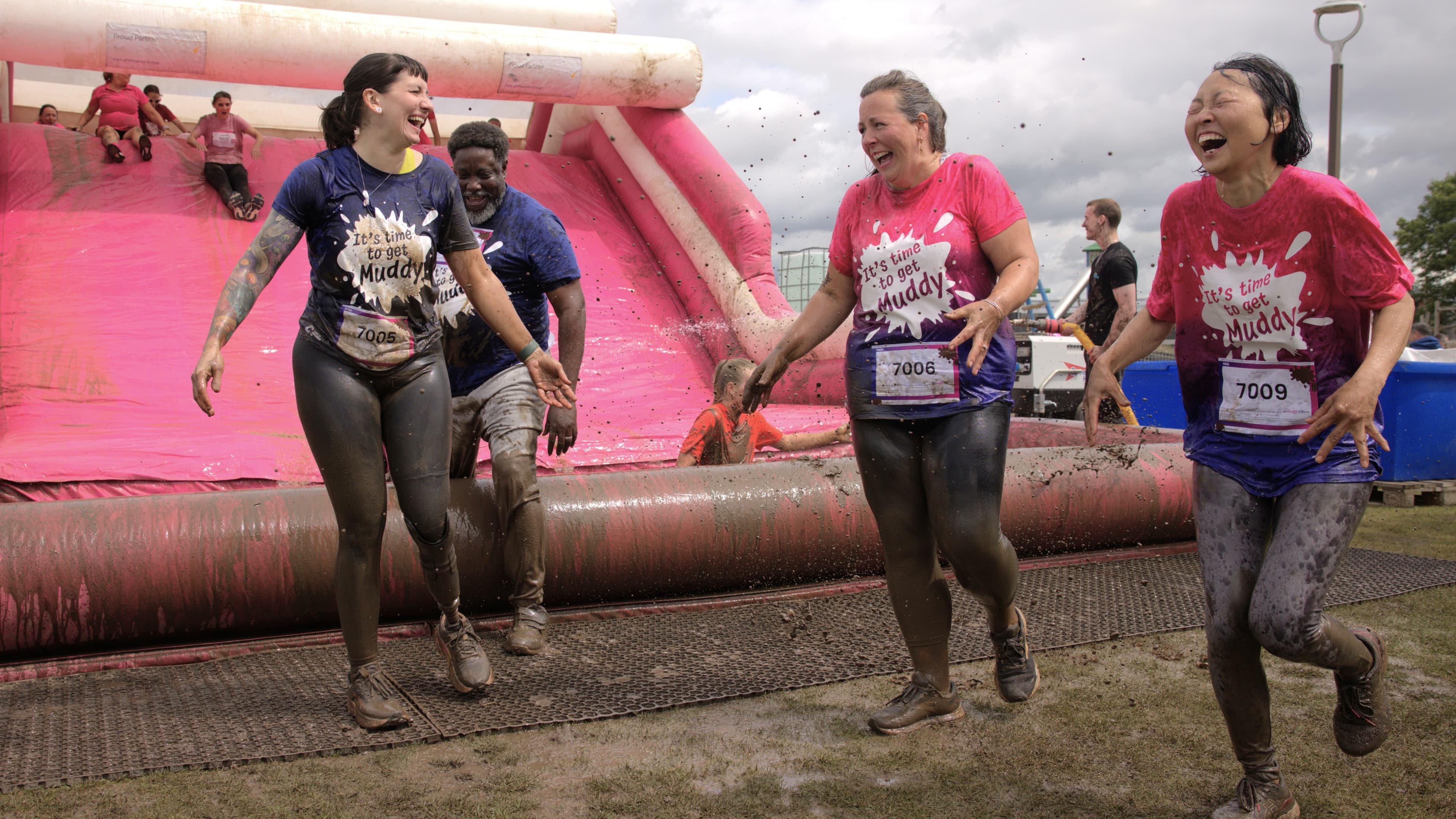 Group of women covered in mud at the bottom of the final muddy obstacle all laughing.